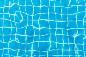 Water ripples on blue tiled swimming pool background. View from above.