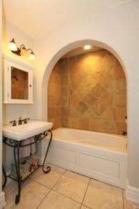 Tub with arch and stone tiles and sink natural bathroom design.