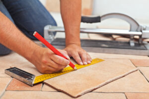 Laying ceramic floor tiles - man hands marking tile to be cut, closeup