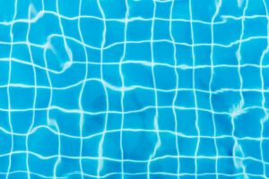 Water ripples on blue tiled swimming pool background. View from above.